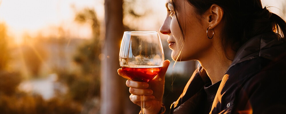 Eine Frau mit einem Glas Rotwein im Sonnenuntergang auf einer Terrasse