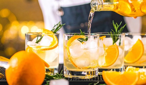 Mehrere Gläser gefüllt mit Eiswürfeln und Orangenscheiben in die Tonic Water gefüllt wird