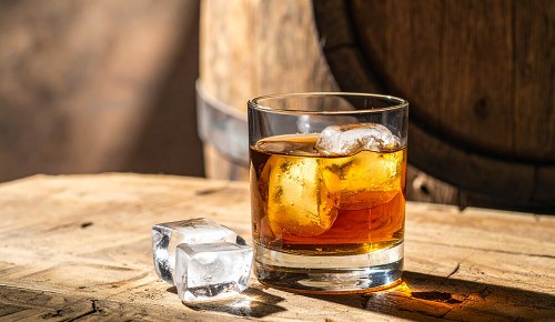 Ein Whiskeyglas gefüllt mit einem braunen Whiskey und einem Eiswürfel