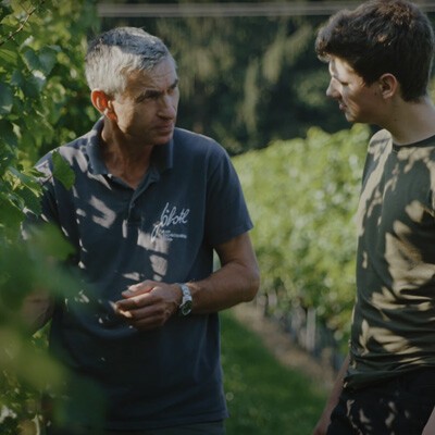 Zwei Mitarbeiter vom Weingut Jöbstl neben einer Weinrebe im Weingarten