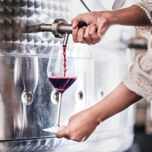 Eine Frau zapft etwas Rotwein aus einem Stahltank in ein Weinglas