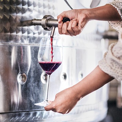 Eine Frau zapft etwas Rotwein aus einem Stahltank in ein Weinglas