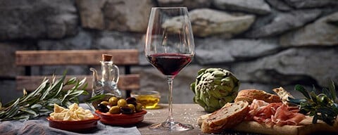 Ein Glas Rotwein auf einem Tisch voller italienischer Snacks
