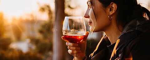 Eine Frau mit einem Glas Rotwein im Sonnenuntergang auf einer Terrasse