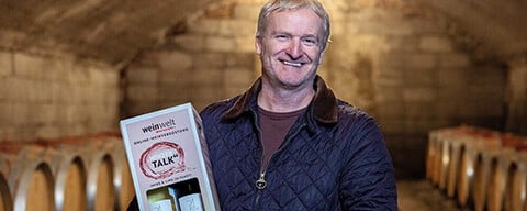 Winzer Paul Achs in einem Weinkeller mit einer INTERSPAR Wein-Tastingbox in der Hand in der Hand