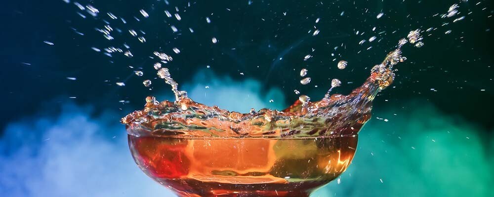 Ein Glas Kaffee aus dem vor einem bunten Hintergrund tropfen fliegen