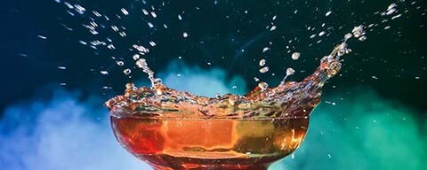 Ein Glas Kaffee aus dem vor einem bunten Hintergrund tropfen fliegen