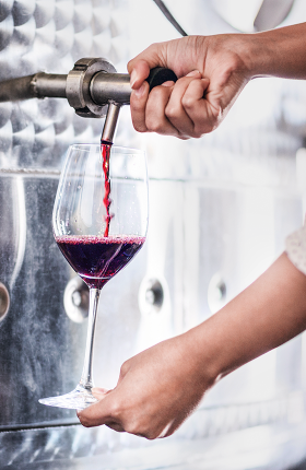 Eine Person beim Anfüllen eines Glases Rotwein aus einem Stahltank