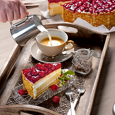 Ein Stück Kuchen und Milch, die in eine Tasse Kaffee gegossen wird