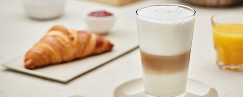 Ein Glas Café Latte und ein Teller mit einem Croissant