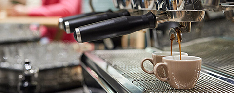 Kaffee fließt aus einer Kaffeemaschine in zwei Tassen