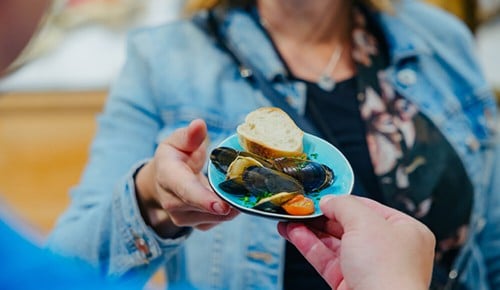 Eine Frau bekommt ein Schälchen mit Muscheln und einem Stück Brot gereicht