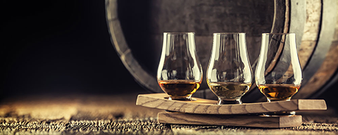 Mehrere Whiskeygläser nebeneinander vor einem Holzfass