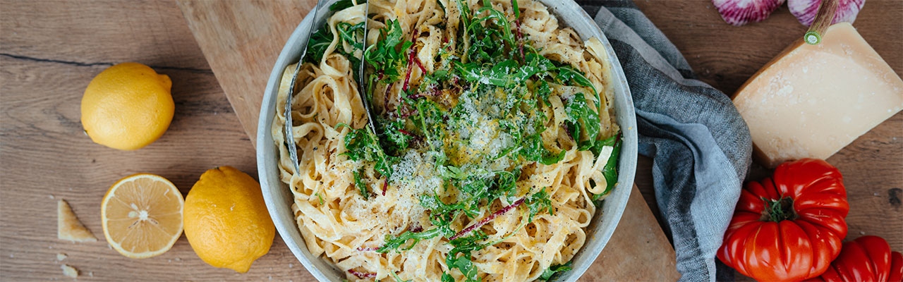Pasta mit Zitronenpesto und Ruccola-Verzierung in einer Schüssel auf einem Holzbrett