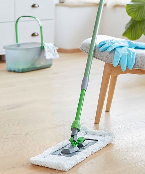 Wischmopp ist an einen Sesselangelehnt auf dem türkise Putzhandschuhe liegen