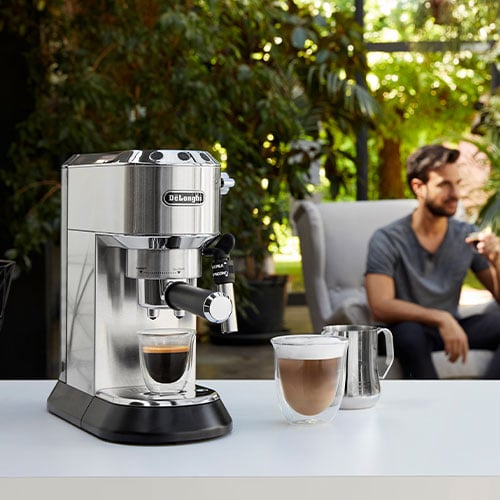 Mann genießt im Garten seinen Kaffee, daneben eine Siebträgermaschine