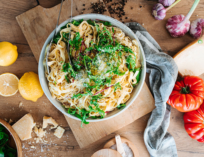 Pasta mit Zitronenpesto und Ruccola-Verzierung in einer Schüssel auf einem Holzbrett