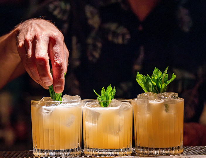 Mann dekoriert Cocktails mit einem Minzblatt
