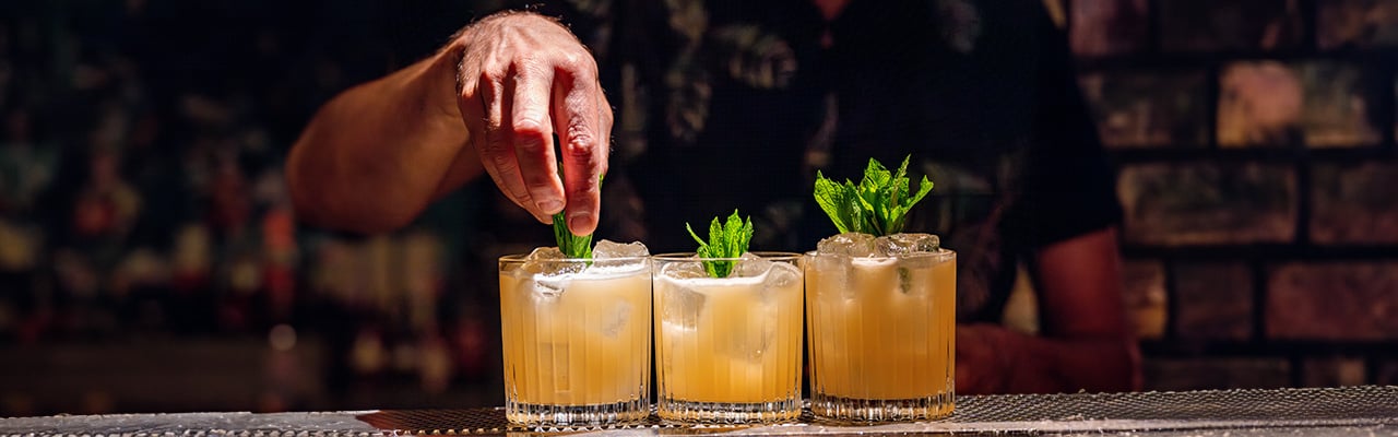 Mann dekoriert Cocktails mit einem Minzblatt